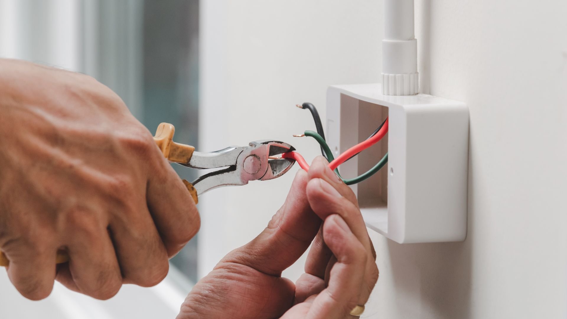 Electrician stripping and connecting colored wires to electrical outlet